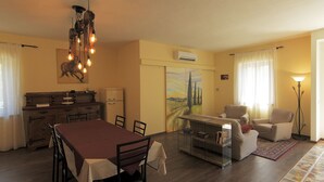 A dining area with a table and chairs, a kitchen with a refrigerator, and a living area with a sofa and armchairs.