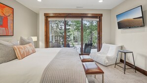 A modern hotel room with a large bed, a seating area, and a view through a glass door to an outdoor deck.