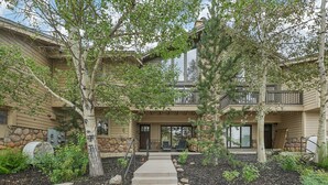 A two-story building with a stone facade, a covered porch, and a landscaped front yard with trees and shrubs.