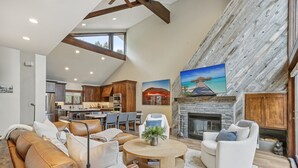 A spacious living area with a high ceiling, wooden beams, a fireplace, and a dining area in the background.
