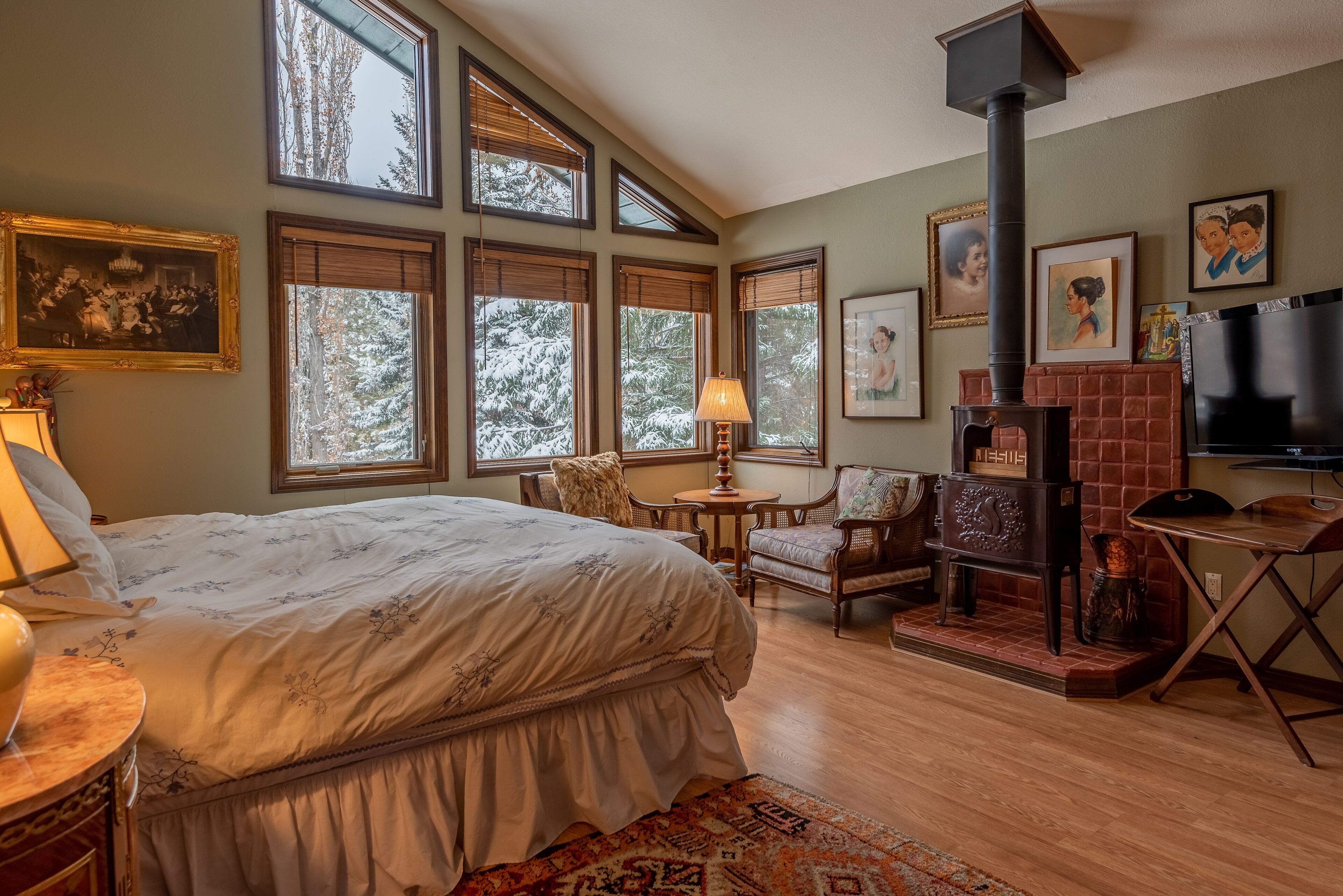 A bedroom with a large bed, multiple windows, a fireplace, and a television.