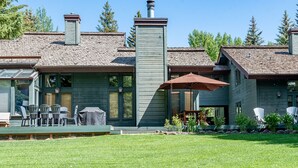 Ein zweistöckiges Haus mit Schornstein, großen Fenstern und einer überdachten Terrasse mit Gartenmöbeln.