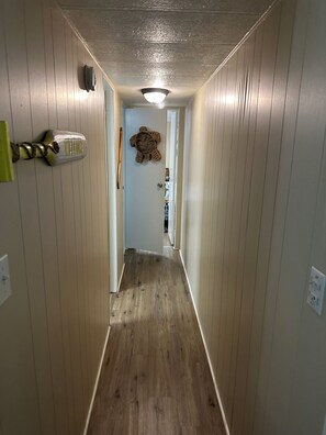 Um corredor estreito com paredes e chão de madeira, que leva a um quarto com porta.