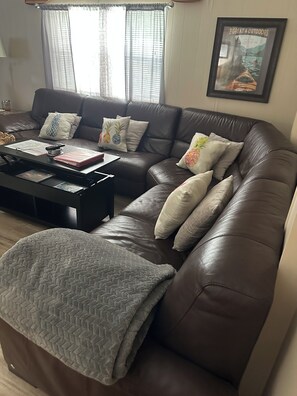 A brown leather sofa with multiple cushions, a coffee table with papers and a calculator, and a framed picture on the wall.