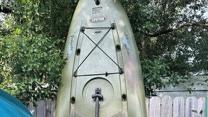 A green paddleboard secured with straps and a leash, with a wooden fence and a blue tarp in the background. - Rainbow River Experience. (Dunnellon)