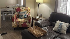 A living room with a floral armchair, a brown leather couch, a woven basket, a lamp, and a ceiling fan. - Rainbow River Experience. (Dunnellon)