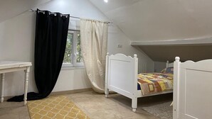 A bedroom with a sloped ceiling, a bed with a colorful quilt, a white desk, and a window with curtains.