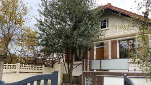 A two-story house with a stone staircase leading to the entrance, a white fence, and a gate.