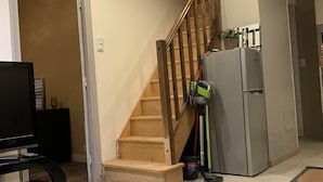A modern kitchen with a wooden staircase, a refrigerator, and a television.