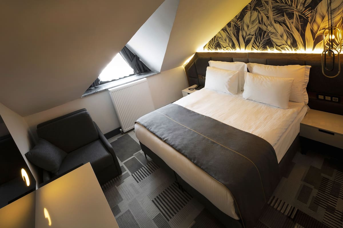Ein modernes Hotelzimmer mit einem großen Bett, einem Schreibtisch, einem Sessel und Blick auf die Stadt durch ein Oberlicht.