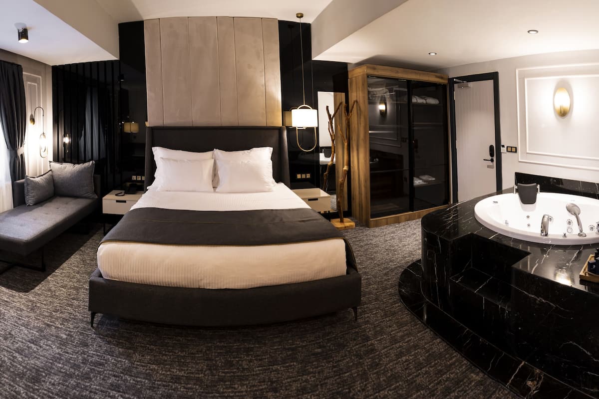 Ein modernes Hotelzimmer mit einem großen Bett, einer Bank, einem Schminktisch mit Spiegel und einem begehbaren Kleiderschrank.