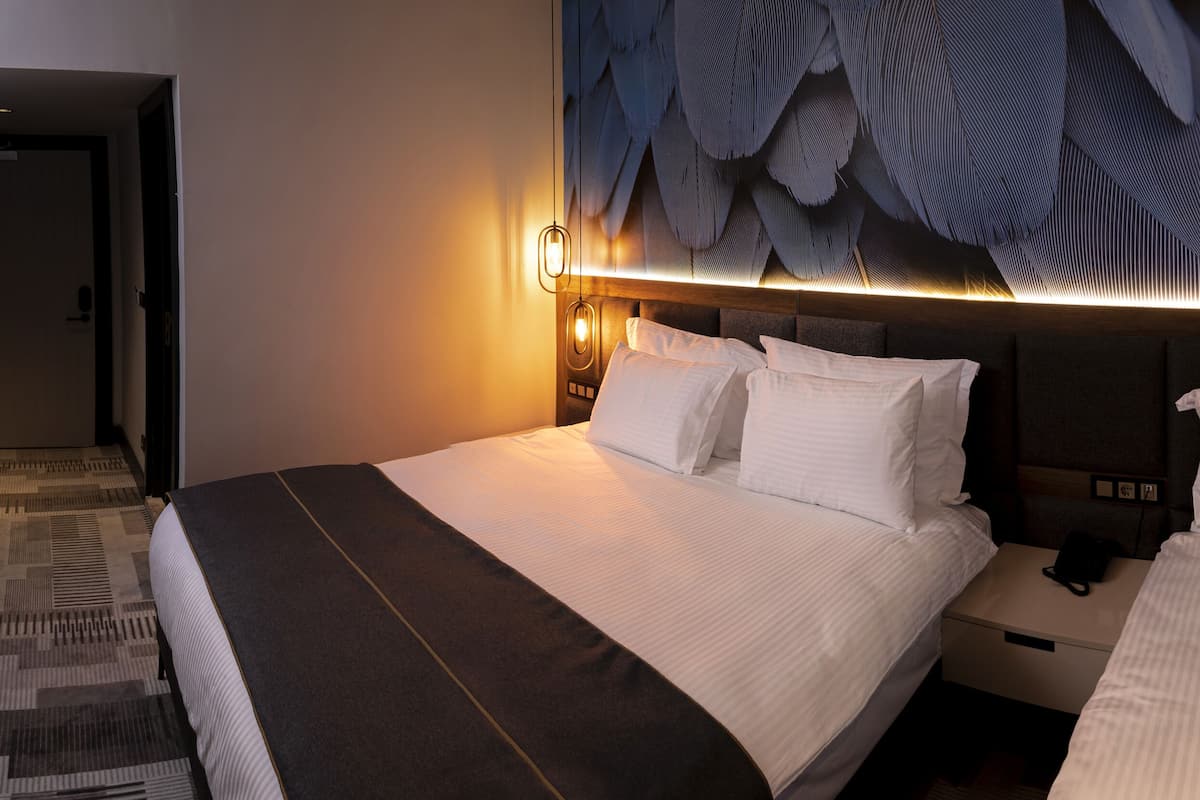 Ein Hotelzimmer mit zwei Betten, einer großen Wandmalerei und einer modernen Leuchte.