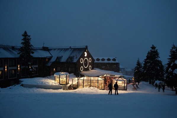 A snow-covered building with a distinctive circular design on the roof, surrounded by snow and trees.