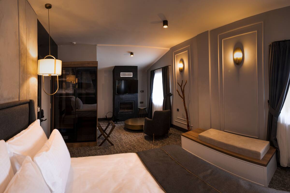 Ein Hotelzimmer mit einem Bett, einer Sitzecke inklusive Sofa und Sesseln, einem Kamin und einem großen Fenster mit Vorhängen.