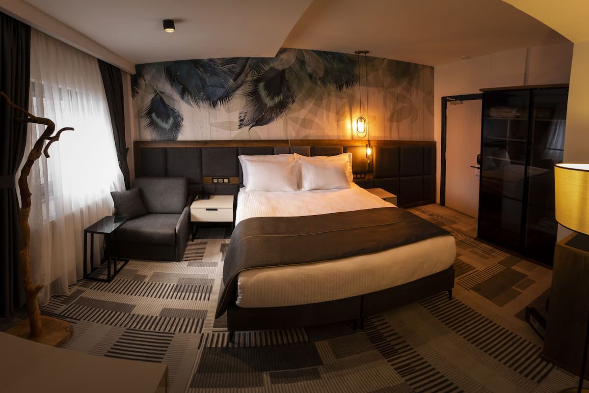 Ein modernes Hotelzimmer mit einem großen Bett, einem Schreibtisch, einem Stuhl, einem Nachttisch, einer Lampe und einer Wand mit einem Blattmuster.
