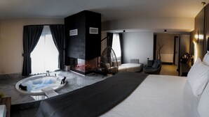 Een moderne hotelkamer met een groot bed, een zithoek met een fauteuil, een open haard en een bad.