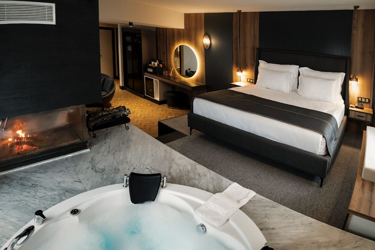 Ein modernes Hotelzimmer mit einem großen Bett, einem Kamin, einem Badezimmer mit Badewanne und einem Schreibtisch mit Spiegel.