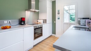 A modern kitchen with white cabinets, a stainless steel range hood, a built-in oven, and a large window providing natural light.