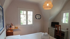 A bedroom with a large bed, a desk, a chair, a window, and a hanging light fixture.