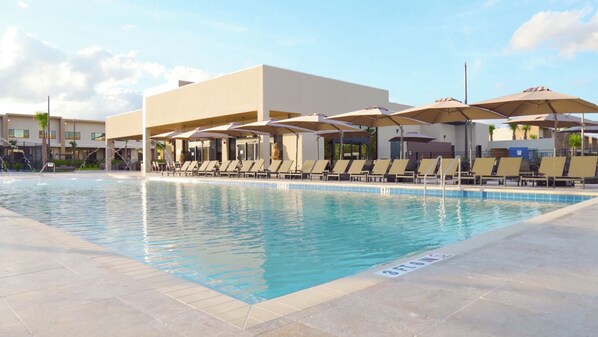 A swimming pool with lounge chairs and umbrellas, surrounded by a building with a flat roof.
