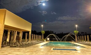 A pool area with lounge chairs and umbrellas, a building with a flat roof, and a night sky with clouds.