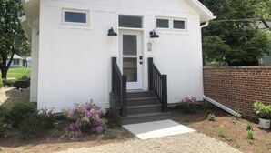 A small, single-story building with a white exterior, a front door, and a staircase leading to the entrance. - Vintage, restored home w/ pool, hot tub & courtyard-just blocks to town & beach (New Buffalo)