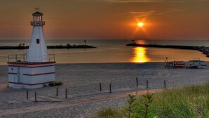 A lighthouse with a red and white striped base, situated on a paved area with a view of the ocean and sunset. - Vintage, restored home w/ pool, hot tub & courtyard-just blocks to town & beach (New Buffalo)