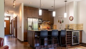 A modern kitchen with wooden cabinets, a stainless steel refrigerator, and a built-in island with bar stools. - 901 Luxury Condos l Dog Friendly (Fernie)