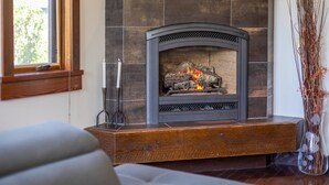 A fireplace with a stone surround, a window to the left, and a vase with branches to the right. - 901 Luxury Condos l Dog Friendly (Fernie)