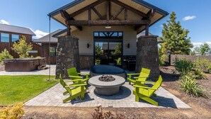 A covered outdoor seating area with a fire pit, surrounded by green chairs, under a stone structure with a wooden roof.