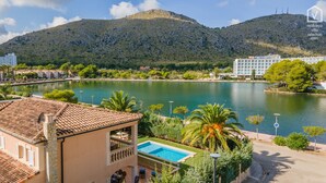 Ein Hotel mit Schwimmbad, umgeben von viel Grün und einem See, mit Bergen im Hintergrund.