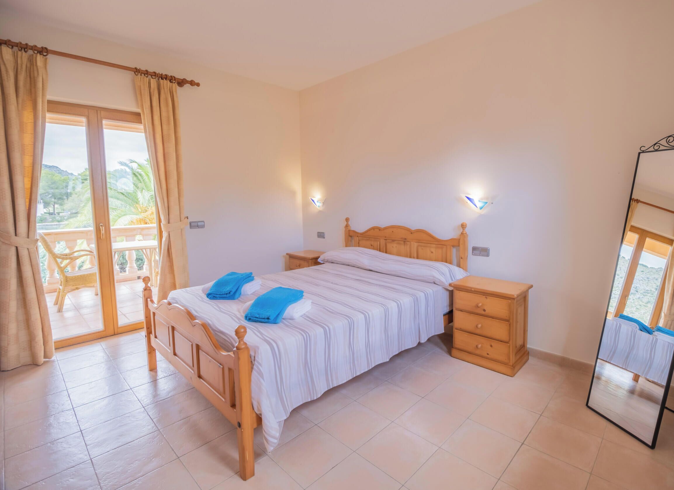 A bedroom with a wooden bed, bedside tables, a mirror, and a sliding glass door to a balcony.