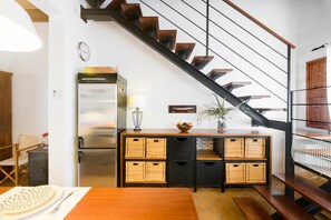 Eine Küche mit einem Holztisch, einem Kühlschrank, Korbwannen, einer Uhr und einer Treppe.