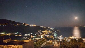 Un pueblo costero iluminado de noche, con edificios brillantes y la luna a la vista.