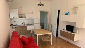 Un apartamento moderno con un sofá rojo, una mesa de comedor de madera y un televisor sobre un mueble blanco.