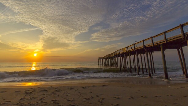 Una playa con un muelle de madera que se adentra en el océano durante el atardecer.