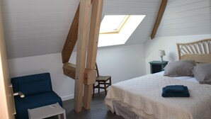 Een slaapkamer met een schuine plafond, dakraam, bed met kussens, stoel en een klein tafeltje.