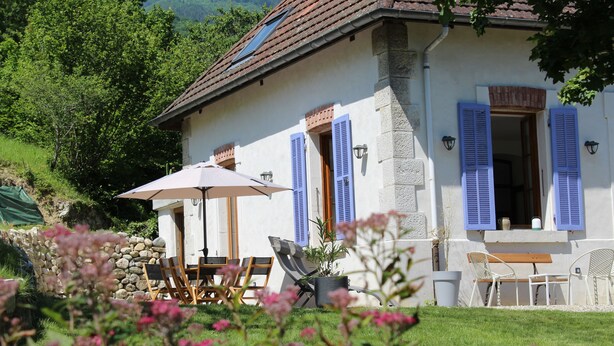 Een huis met een stenen gevel, blauwe luiken en terras met parasols.