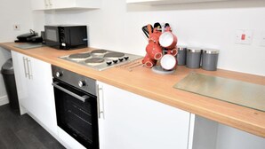A modern kitchen with white cabinets, a wooden countertop, a microwave, a stove, and a coffee machine. - Townhouse @ 50 Birks Street Stoke (Stoke-on-Trent)
