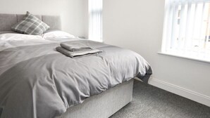 A bedroom with a bed, pillows, and a window. - Townhouse @ 50 Birks Street Stoke (Stoke-on-Trent)
