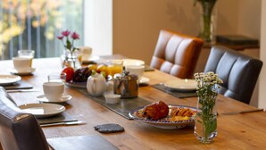 A breakfast table set with plates, cups, a teapot, a vase with flowers, and a fruit bowl.
