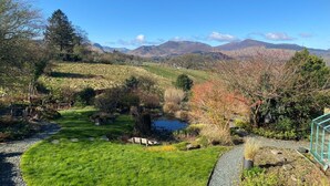A rural landscape with a pond, grassy areas, and a view of distant mountains.