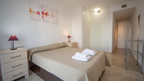 A hotel room with a bed, bedside tables, a wardrobe, and a bathroom with a shower and a towel rack. - Marina Real apto 303 (Manilva)