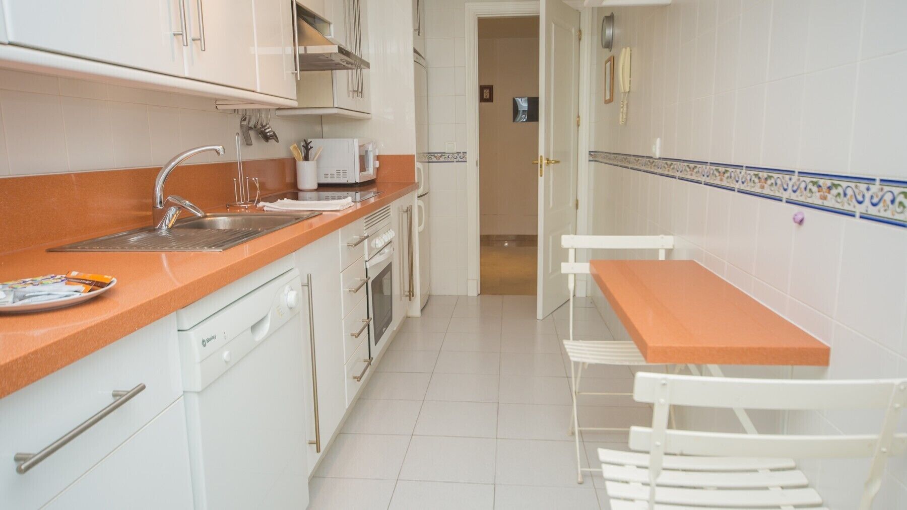A compact kitchen with white cabinets, a sink, and a small dining area with a table and chairs.