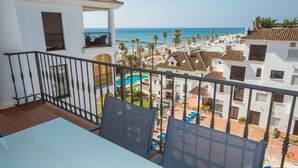 Een balkon met uitzicht op een zwembad, palmbomen en een strand.