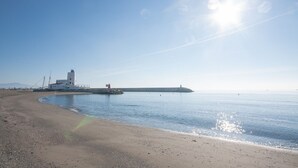 A coastal scene with a lighthouse, calm sea, and a sandy beach. - Marina Real number 254 (Manilva)