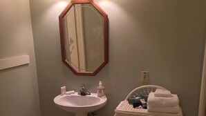 A bathroom with a pedestal sink, a mirror with a wooden frame, and a small wicker chair with towels. - Spacious room with private entrance near Bidwell Park! (Chico)