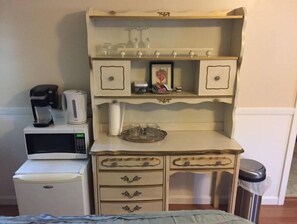 Compact kitchenette with microwave, refrigerator, and coffee maker, featuring a shelf for storage and two drawers.