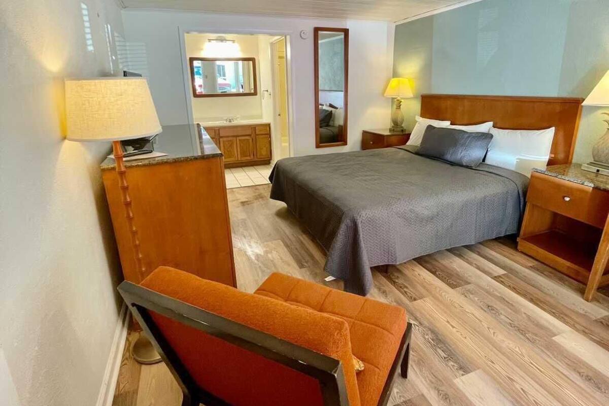 A hotel room with a bed, a desk, a chair, a nightstand, and a mirror.