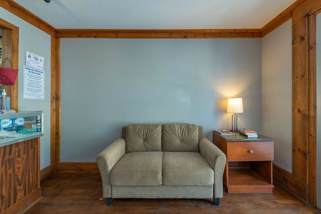 A room with a beige sofa, a wooden desk with a lamp, and a sign indicating dogs are welcome.